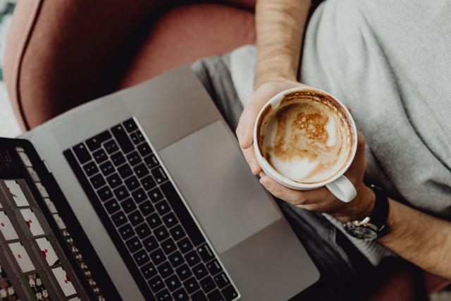 A man's hand is shown holding a coffee cup near a computer