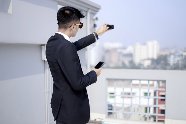 A business man poses for a selfie while pretending to look casually at his phone