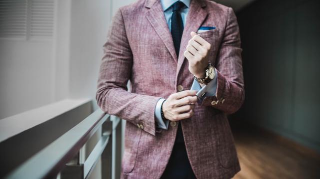 A well-dressed man in a business suit tugs on his cuff while showing off an expensive watch